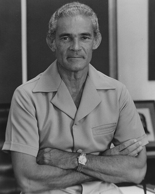 A black-and-white portrait of a silver-haired man in a light Kareeba bush jacket, arms folded, a watch on his wrist.