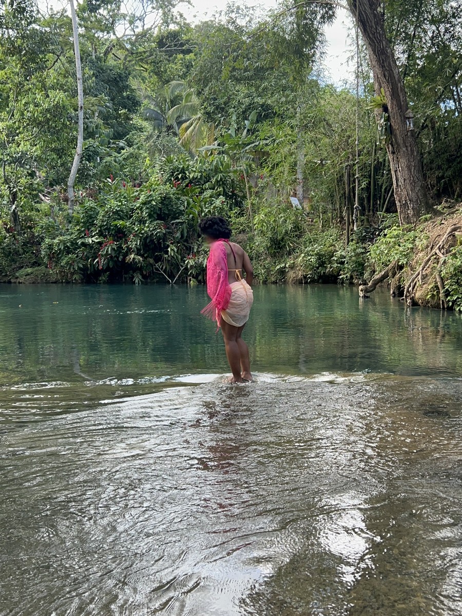 A woman in a pink sheer wrap wades into the turquoise river, back to camera