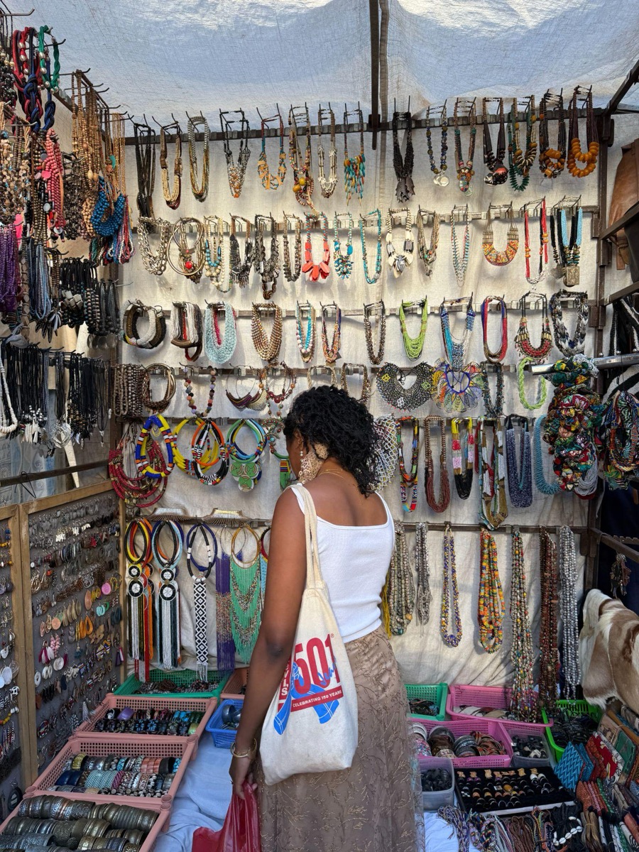 A woman seen from behind at a wall of hanging beaded necklaces